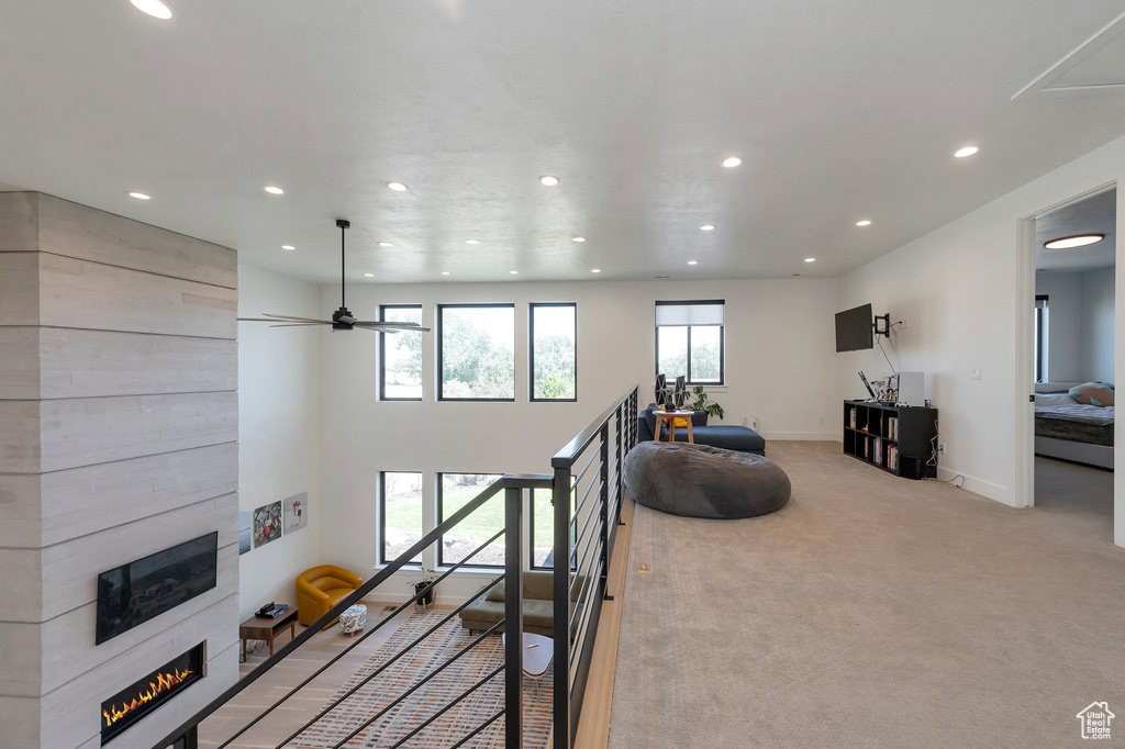 Staircase with a fireplace, light colored carpet, and ceiling fan