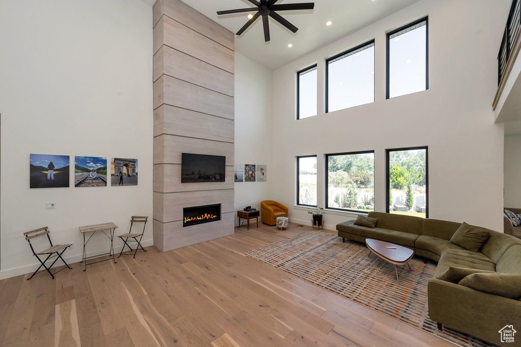 Living room featuring a towering ceiling, a tiled fireplace, light hardwood / wood-style flooring, and ceiling fan