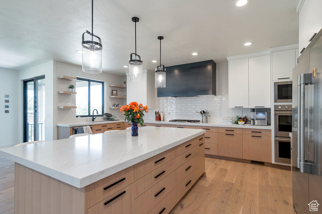 Kitchen featuring light hardwood / wood-style floors, hanging light fixtures, tasteful backsplash, and wall chimney range hood