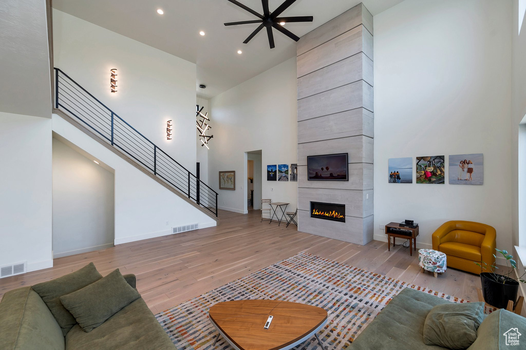 Living room featuring ceiling fan, a fireplace, hardwood / wood-style flooring, and a towering ceiling