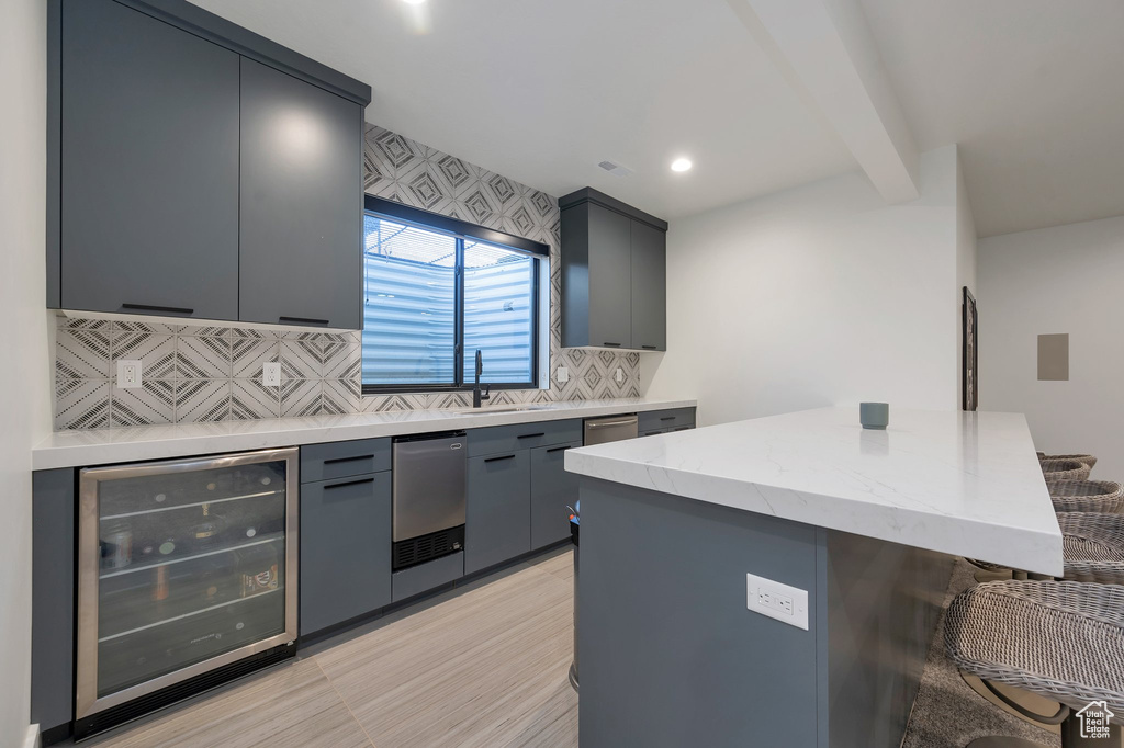 Kitchen featuring wine cooler, a kitchen island, decorative backsplash, sink, and gray cabinetry