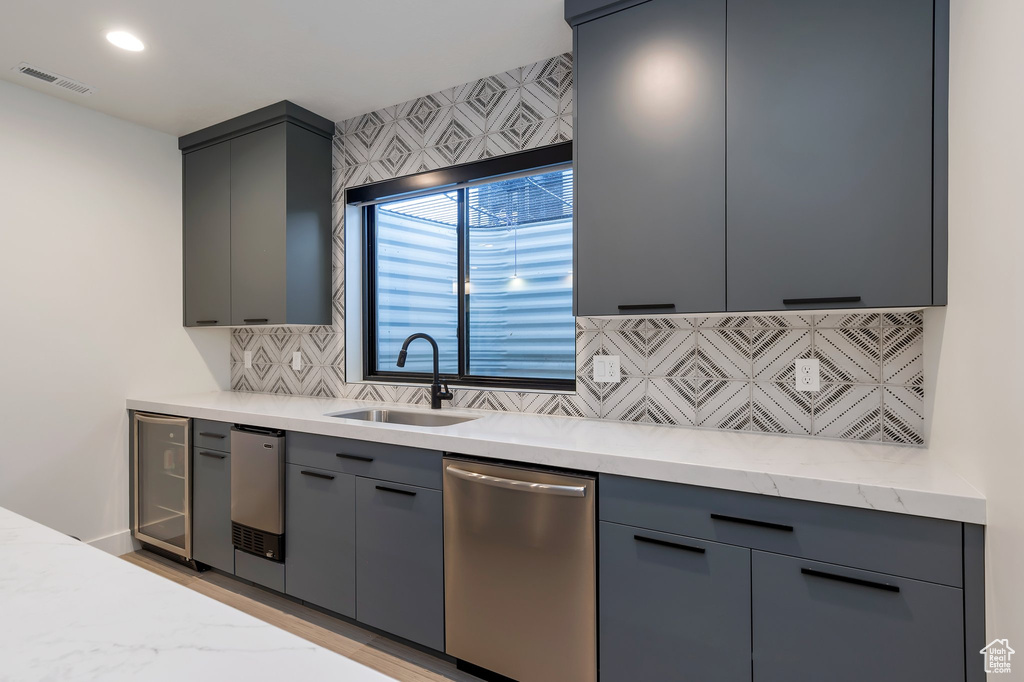 Kitchen featuring stainless steel dishwasher, tasteful backsplash, sink, light stone counters, and gray cabinetry