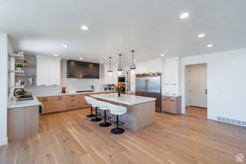 Kitchen featuring built in appliances, backsplash, light wood-type flooring, and a center island