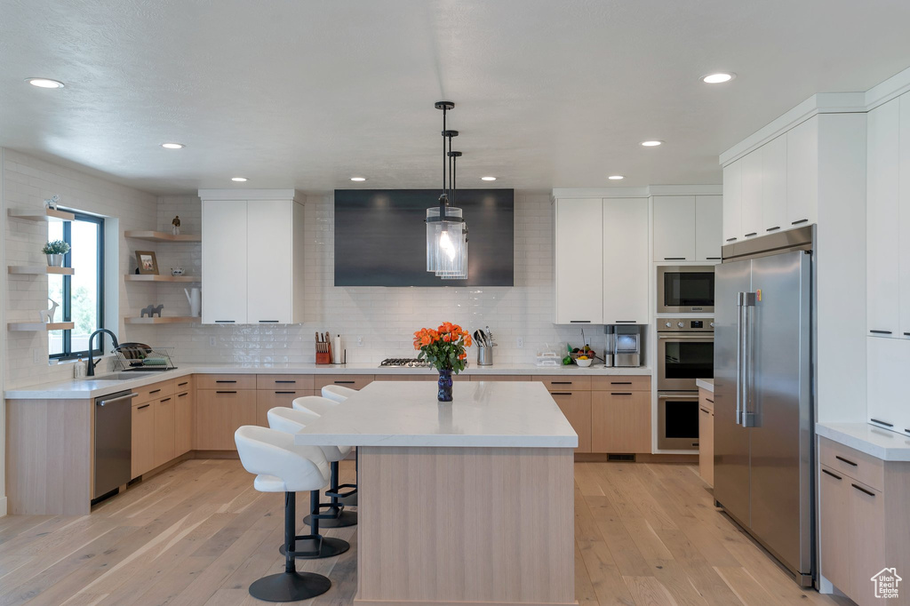 Kitchen with built in appliances, pendant lighting, a kitchen island, decorative backsplash, and light wood-type flooring