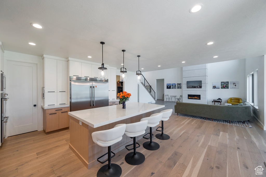 Kitchen with light hardwood / wood-style flooring, white cabinets, a fireplace, built in fridge, and a center island