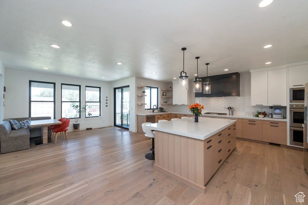 Kitchen featuring tasteful backsplash, decorative light fixtures, light hardwood / wood-style floors, a center island, and range hood