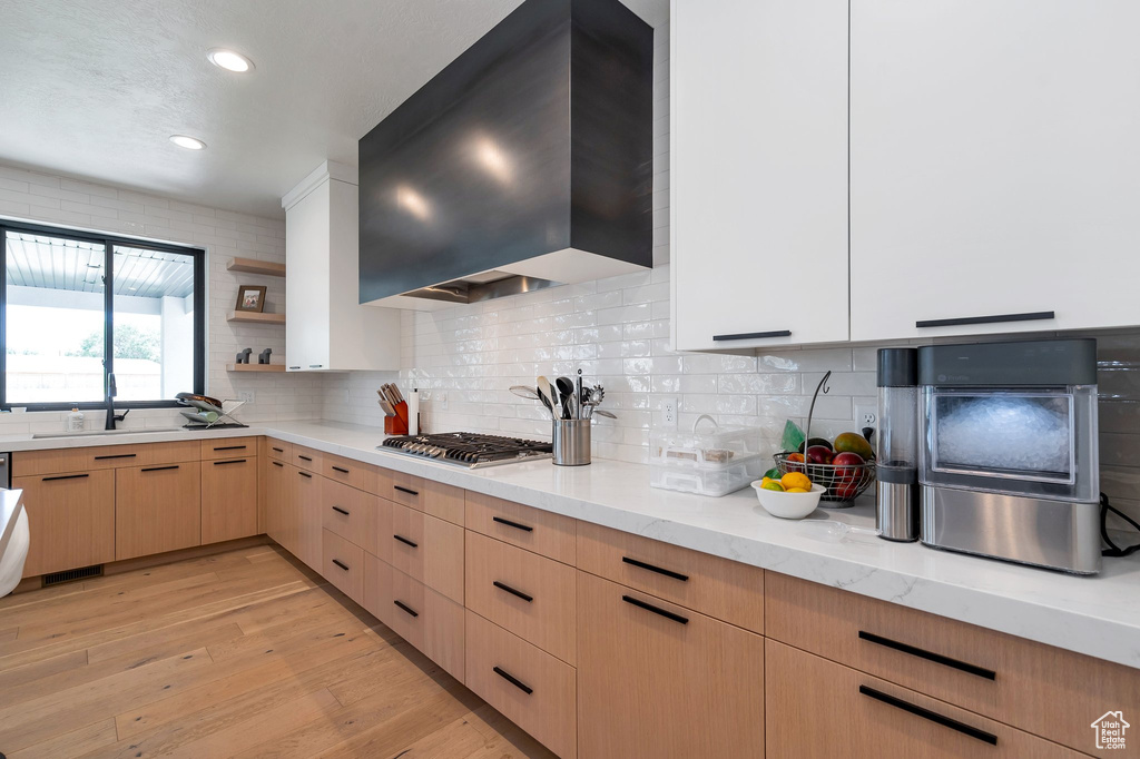 Kitchen featuring light brown cabinetry, decorative backsplash, stainless steel gas stovetop, light stone counters, and light hardwood / wood-style floors