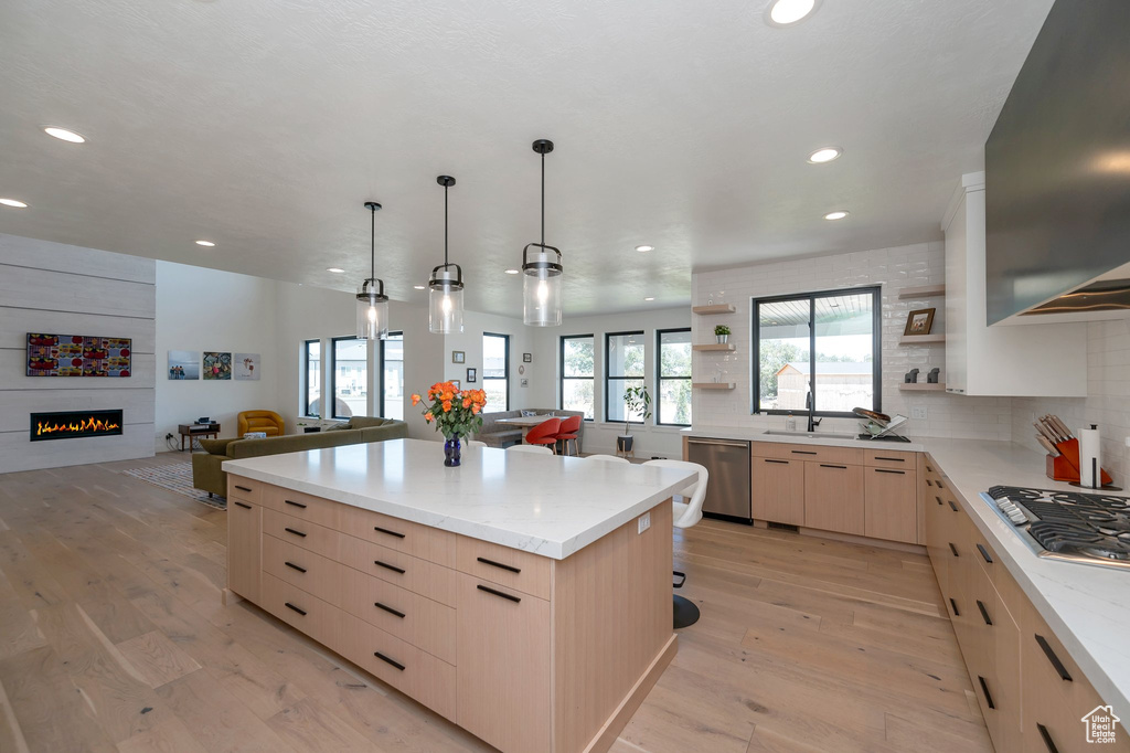 Kitchen featuring appliances with stainless steel finishes, light hardwood / wood-style floors, a large fireplace, light brown cabinetry, and a center island