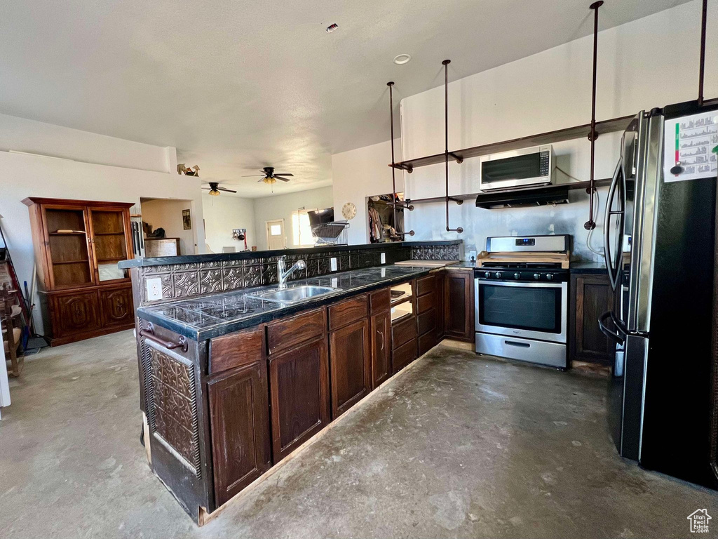 Kitchen with concrete floors, kitchen peninsula, ceiling fan, appliances with stainless steel finishes, and sink