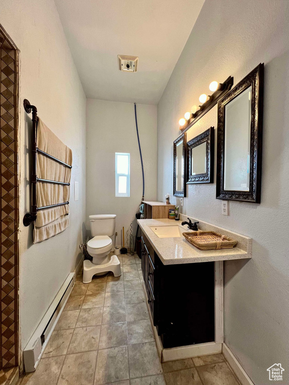 Bathroom featuring vanity, toilet, baseboard heating, and tile patterned flooring