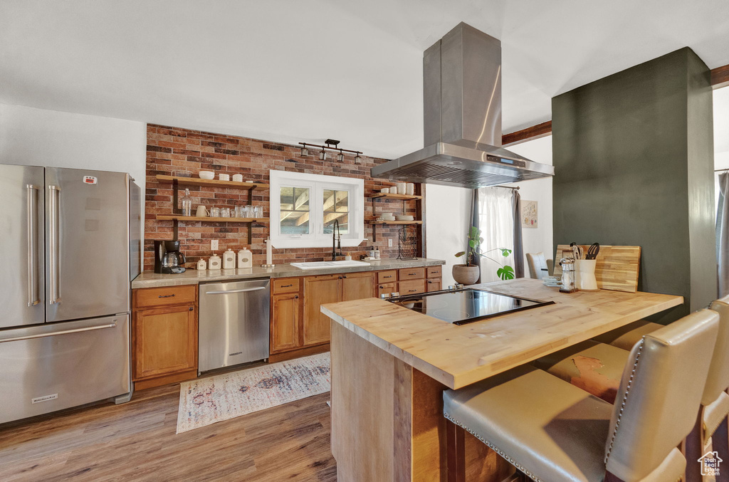 Kitchen featuring sink, light hardwood / wood-style floors, appliances with stainless steel finishes, island range hood, and wood counters