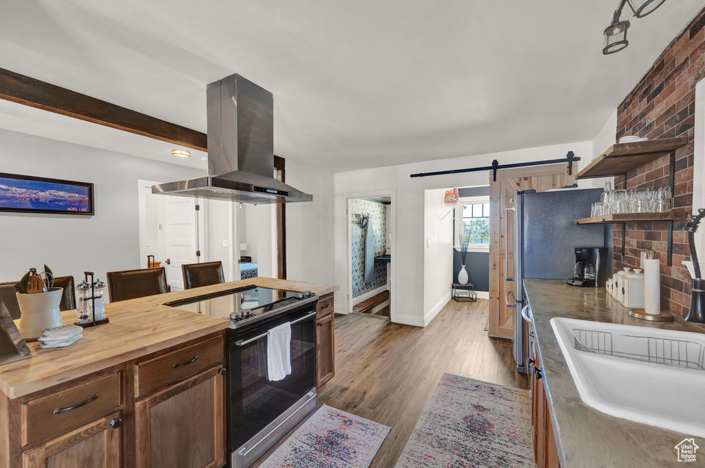 Kitchen featuring hardwood / wood-style floors, island range hood, wooden counters, a barn door, and stainless steel electric range oven