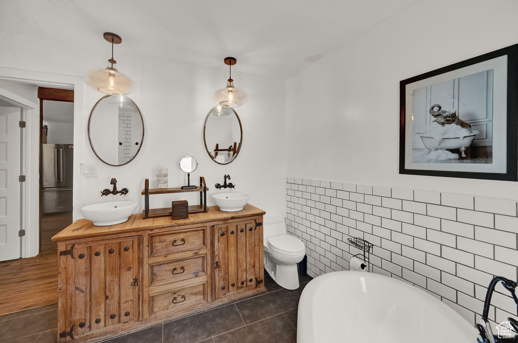 Bathroom featuring tile patterned floors, tile walls, dual vanity, a bathtub, and toilet