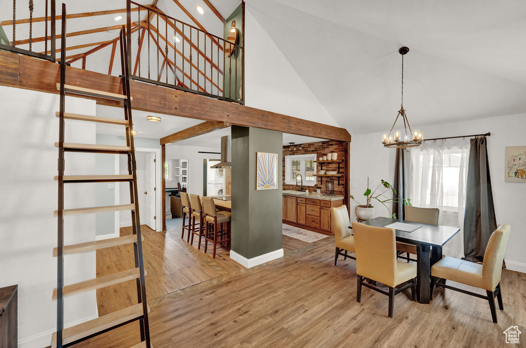 Dining space with an inviting chandelier, high vaulted ceiling, sink, and light hardwood / wood-style flooring