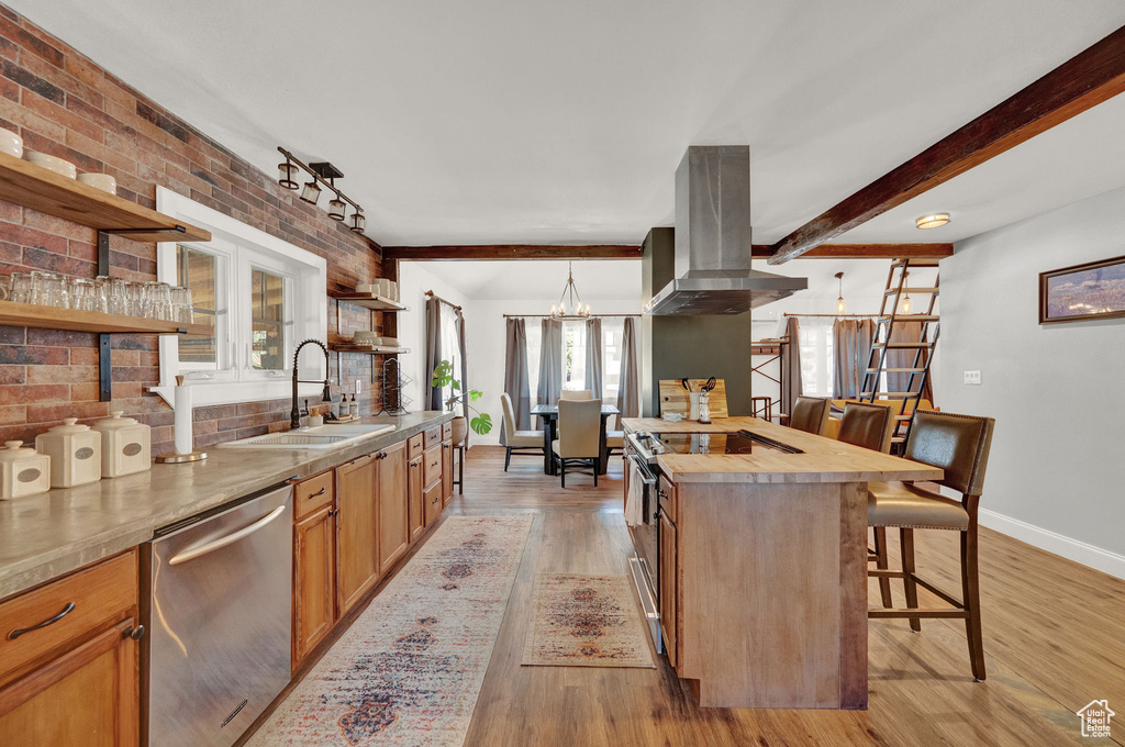 Kitchen featuring appliances with stainless steel finishes, a breakfast bar area, island range hood, sink, and decorative light fixtures