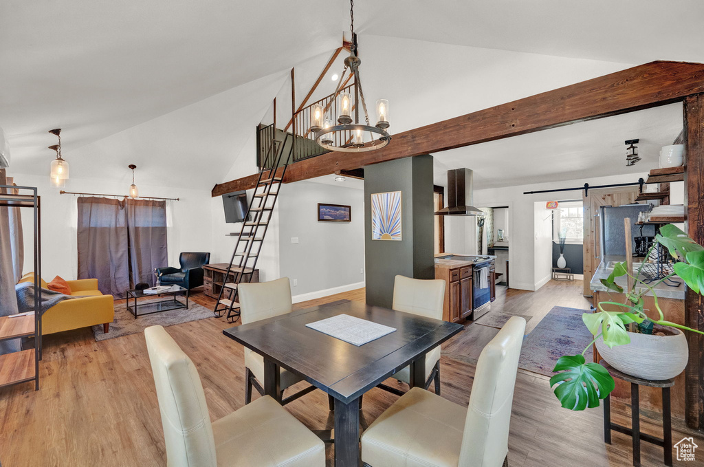 Dining area with light hardwood / wood-style floors, a chandelier, lofted ceiling, and a barn door