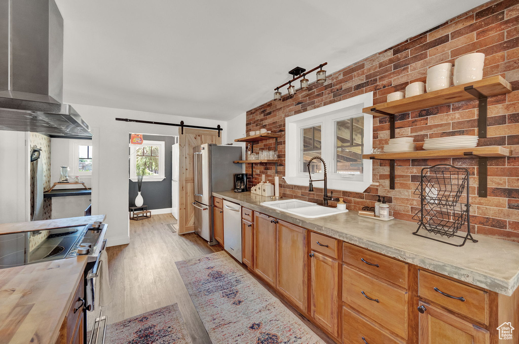 Kitchen featuring electric stove, wall chimney exhaust hood, sink, a barn door, and light hardwood / wood-style floors