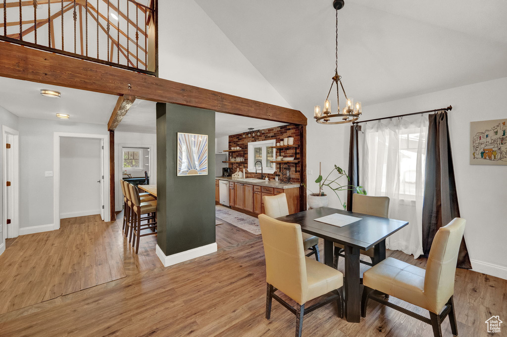 Dining area with an inviting chandelier, high vaulted ceiling, sink, and light wood-type flooring