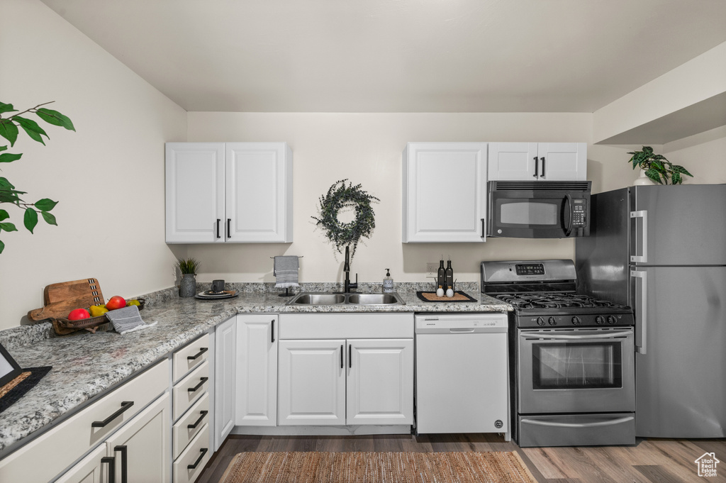 Kitchen featuring white cabinetry, stainless steel appliances, sink, light stone counters, and dark wood-type flooring