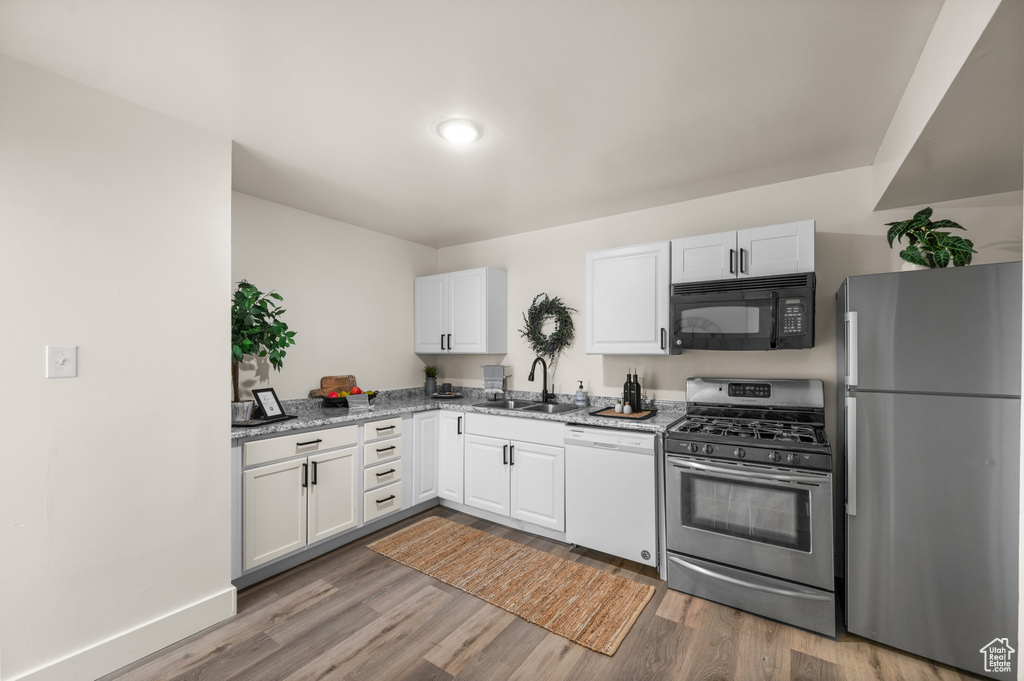 Kitchen with appliances with stainless steel finishes, hardwood / wood-style floors, sink, light stone counters, and white cabinetry