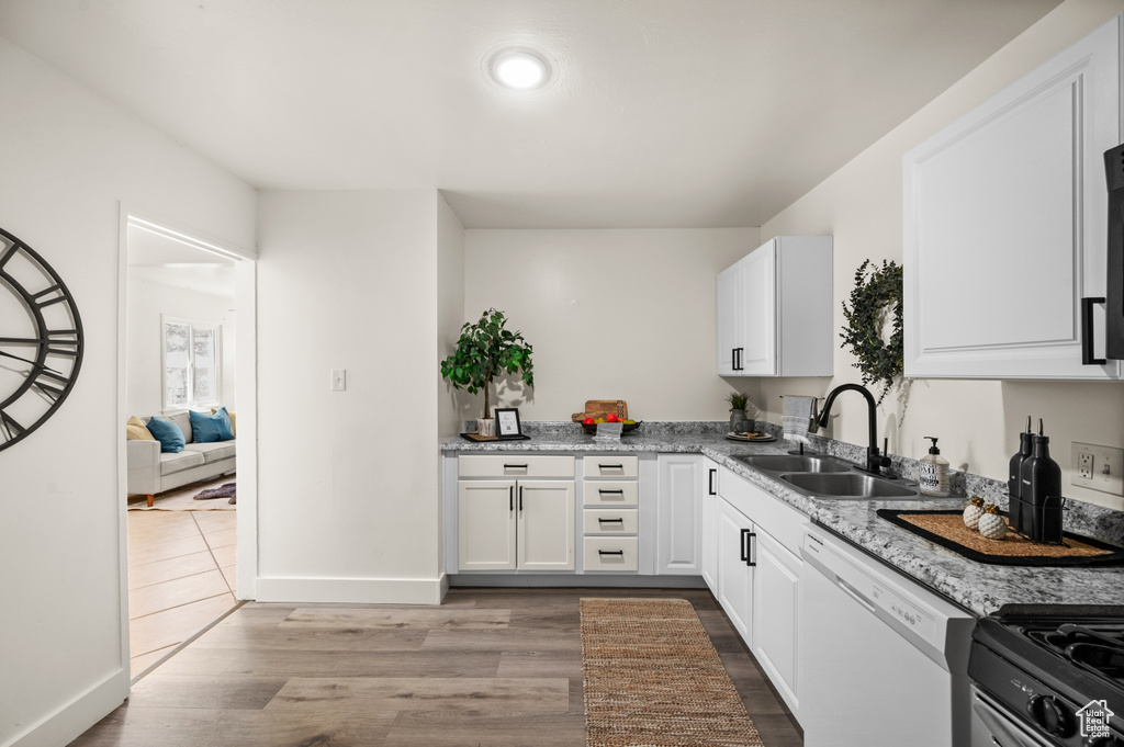 Kitchen featuring sink, dishwasher, hardwood / wood-style flooring, and white cabinets