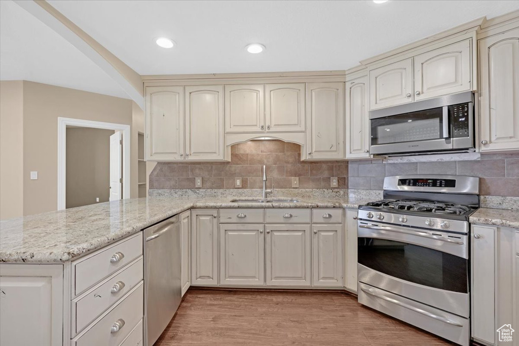 Kitchen featuring stainless steel appliances, decorative backsplash, sink, light hardwood / wood-style flooring, and kitchen peninsula