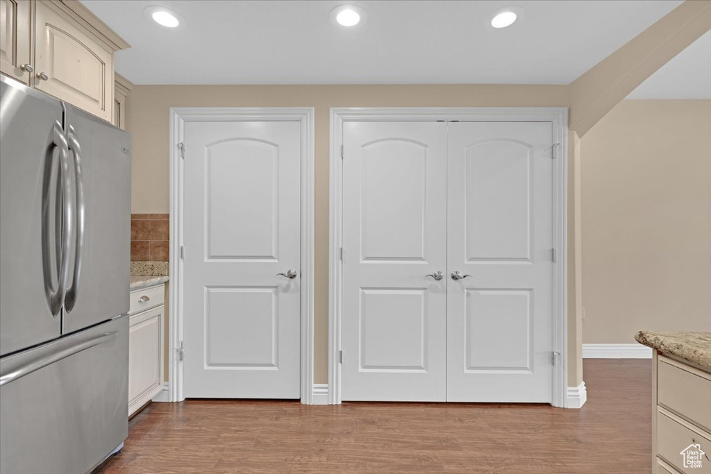 Kitchen with stainless steel fridge, light hardwood / wood-style flooring, cream cabinetry, and light stone countertops