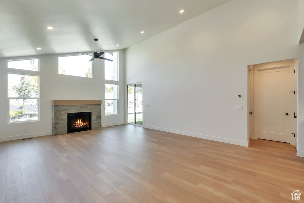 Unfurnished living room with a stone fireplace, light wood-type flooring, and a wealth of natural light