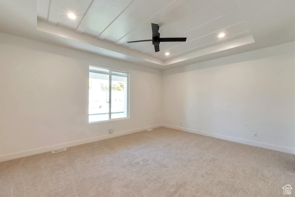 Carpeted spare room featuring ceiling fan and a raised ceiling