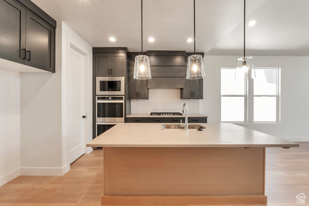 Kitchen with a kitchen island with sink, light hardwood / wood-style floors, sink, and black microwave