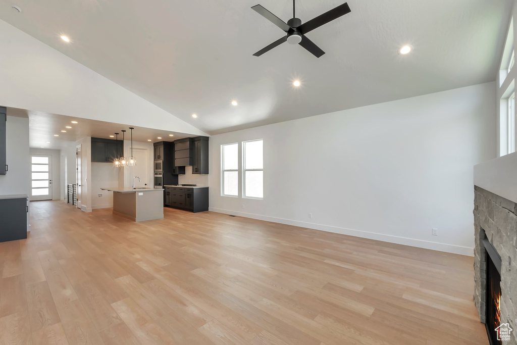 Unfurnished living room with a fireplace, ceiling fan with notable chandelier, high vaulted ceiling, sink, and light hardwood / wood-style floors