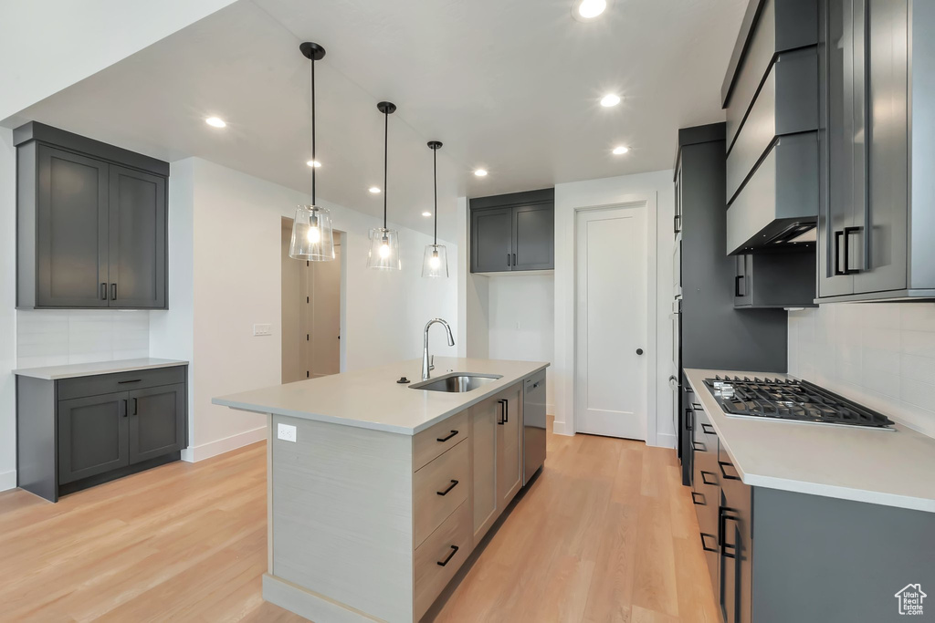 Kitchen with light hardwood / wood-style floors, sink, a center island with sink, and backsplash