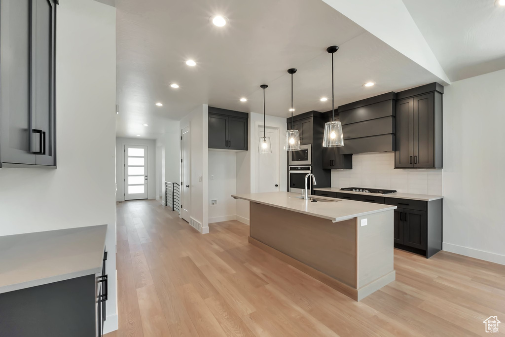 Kitchen featuring premium range hood, tasteful backsplash, gas cooktop, light hardwood / wood-style floors, and a kitchen island with sink