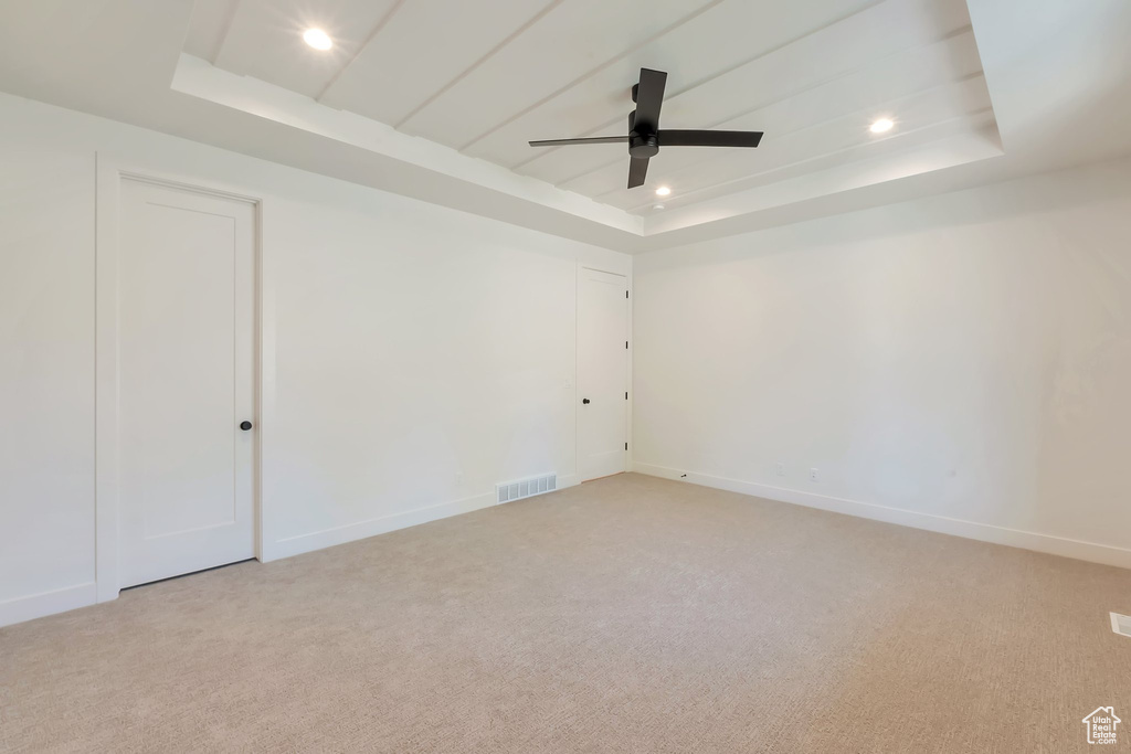 Carpeted empty room with ceiling fan and a tray ceiling