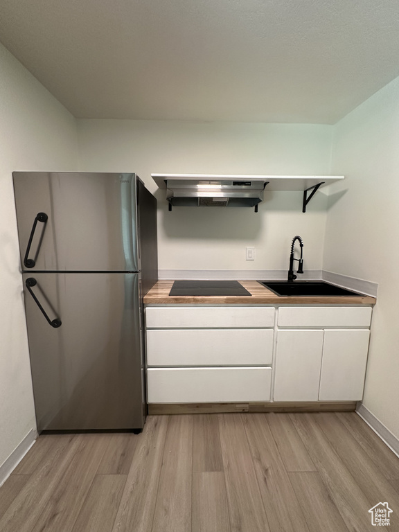 Kitchen featuring light hardwood / wood-style flooring, stainless steel fridge, sink, white cabinetry, and wall chimney exhaust hood