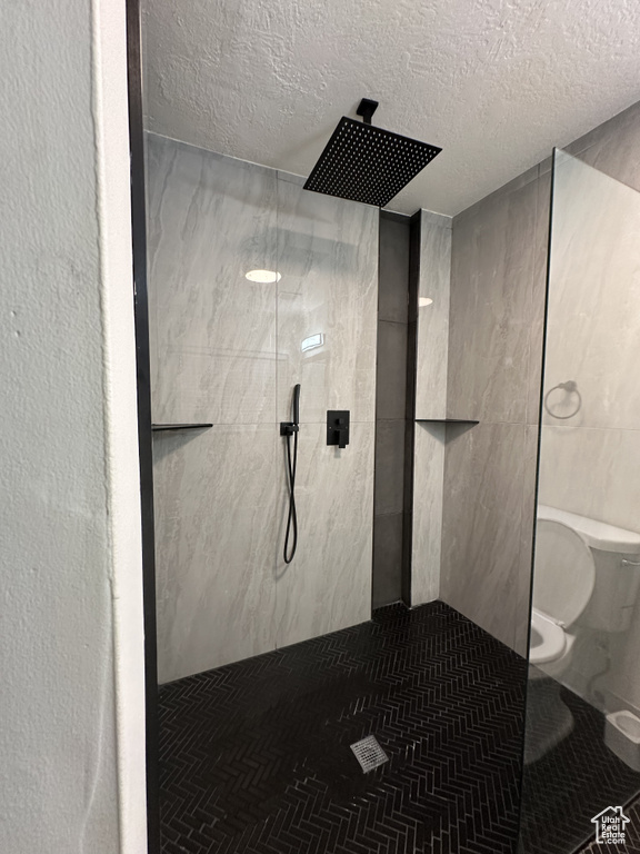 Bathroom with toilet, a tile shower, and a textured ceiling