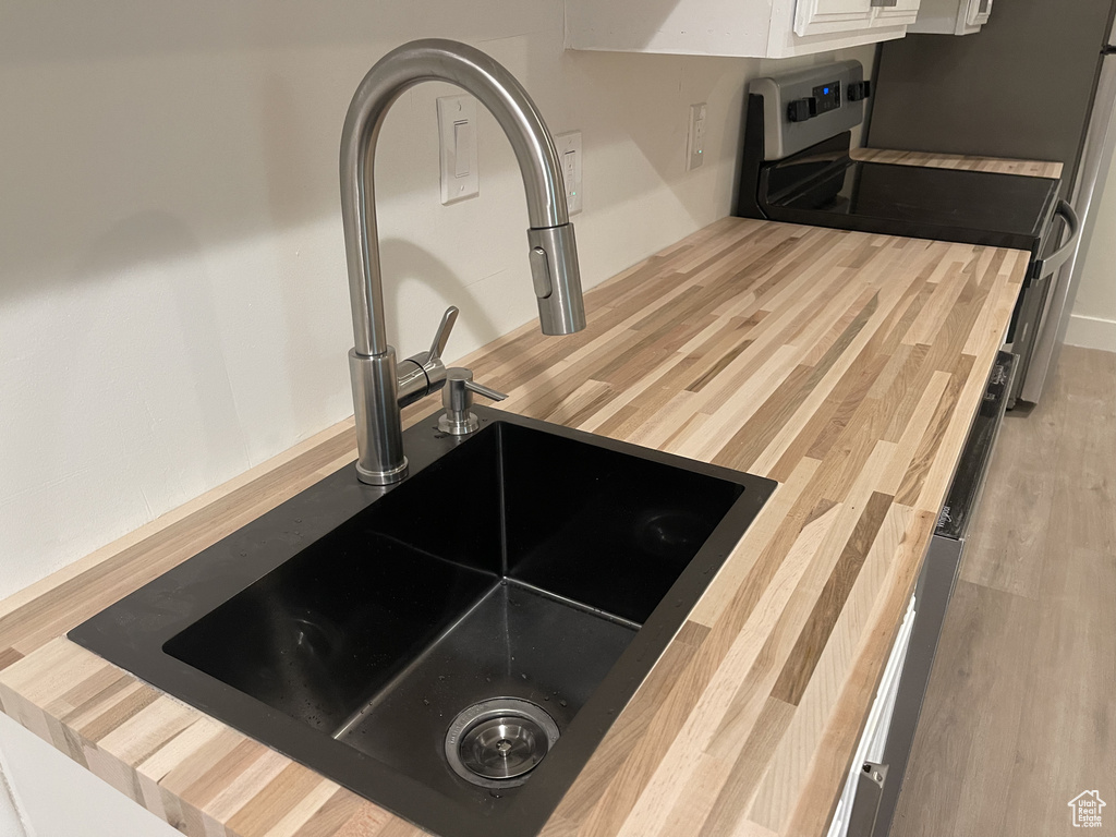 Details with stainless steel electric range, wooden counters, white cabinets, sink, and light hardwood / wood-style flooring