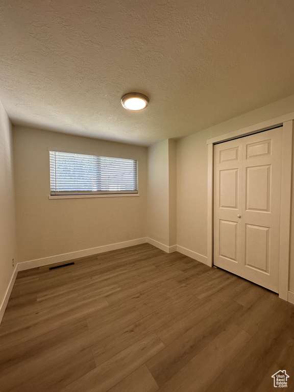 Unfurnished bedroom featuring dark hardwood / wood-style flooring, a closet, and a textured ceiling