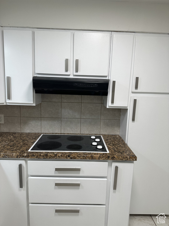 Kitchen with white cabinetry, backsplash, dark stone counters, and ventilation hood