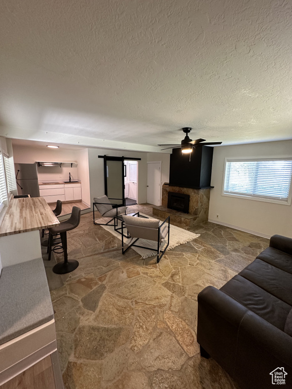 Living room featuring a fireplace, hardwood / wood-style flooring, ceiling fan, a barn door, and a textured ceiling