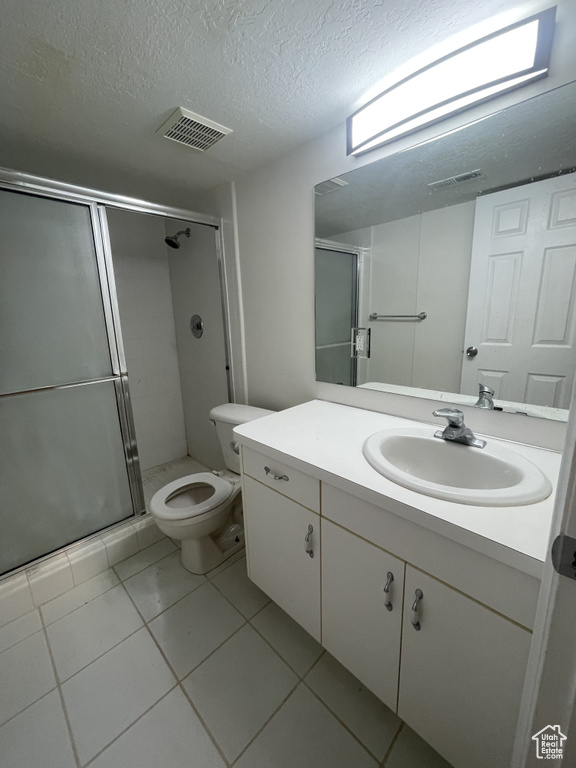 Bathroom featuring tile patterned flooring, a textured ceiling, an enclosed shower, toilet, and vanity