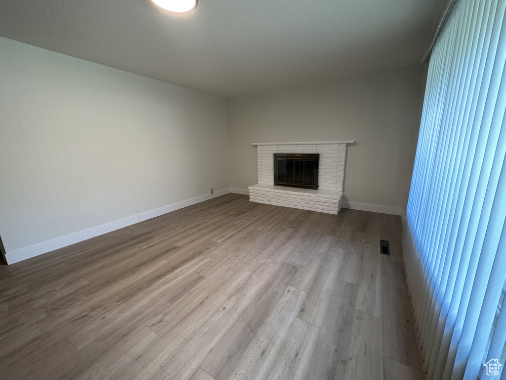 Unfurnished living room with wood-type flooring and a brick fireplace