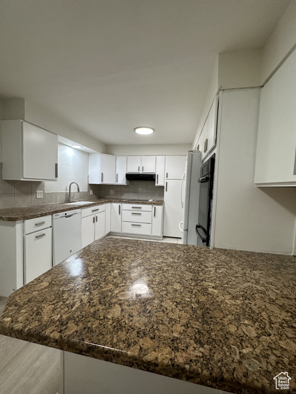 Kitchen featuring white cabinetry, dishwasher, dark stone countertops, and tasteful backsplash