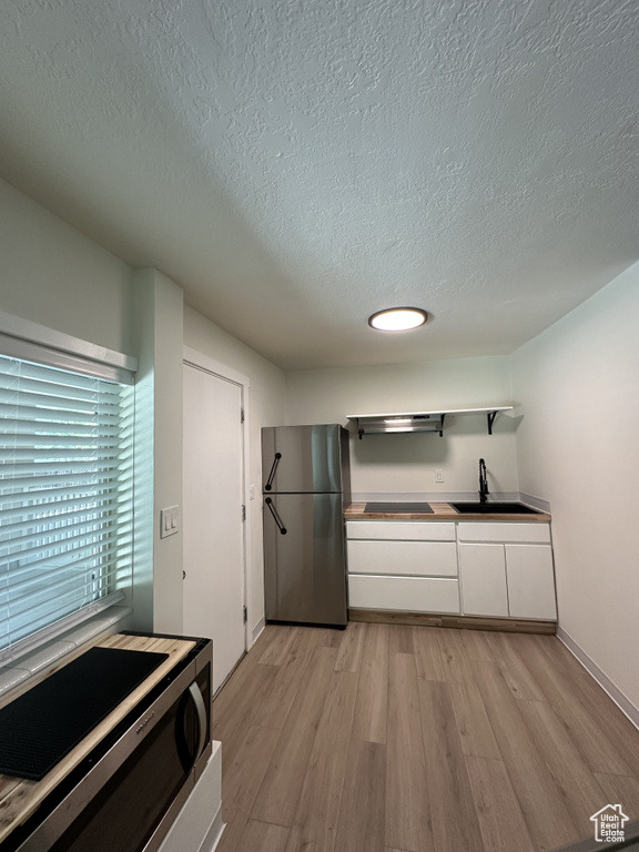 Kitchen featuring stainless steel appliances, white cabinets, light wood-type flooring, sink, and a textured ceiling