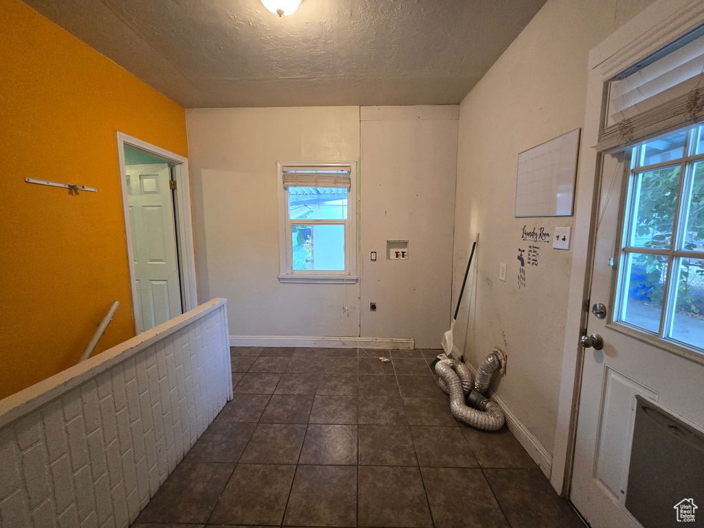 Clothes washing area with hookup for a washing machine, dark tile patterned floors, hookup for an electric dryer, and a textured ceiling