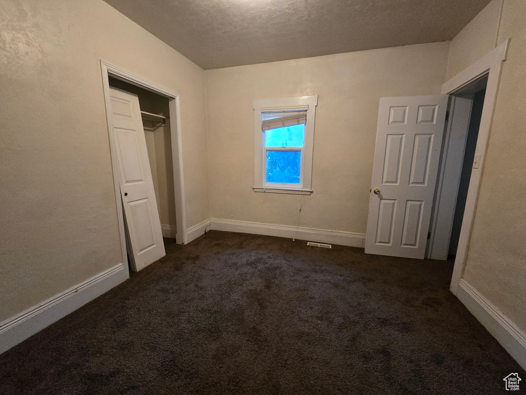 Unfurnished bedroom with dark carpet, a closet, and a textured ceiling