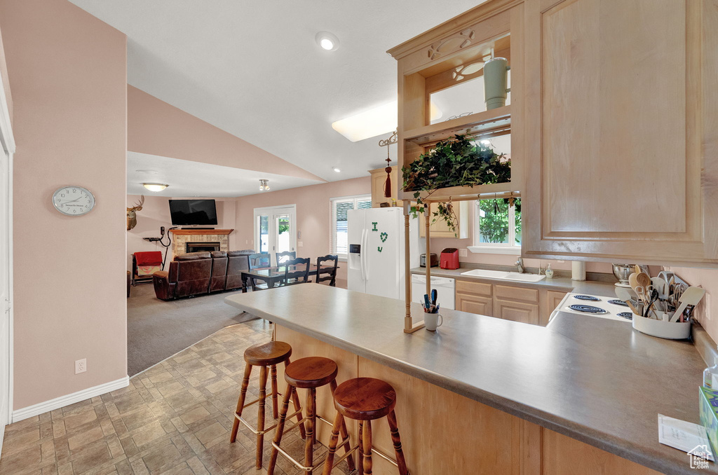 Kitchen with a breakfast bar, white appliances, light colored carpet, vaulted ceiling, and sink