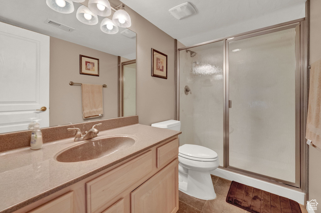 Bathroom featuring a shower with shower door, vanity, tile patterned flooring, and toilet