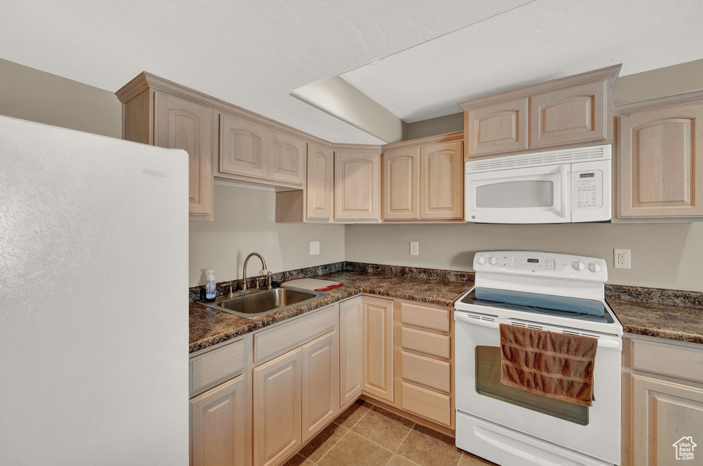 Kitchen with light tile patterned floors, light brown cabinets, white appliances, and sink