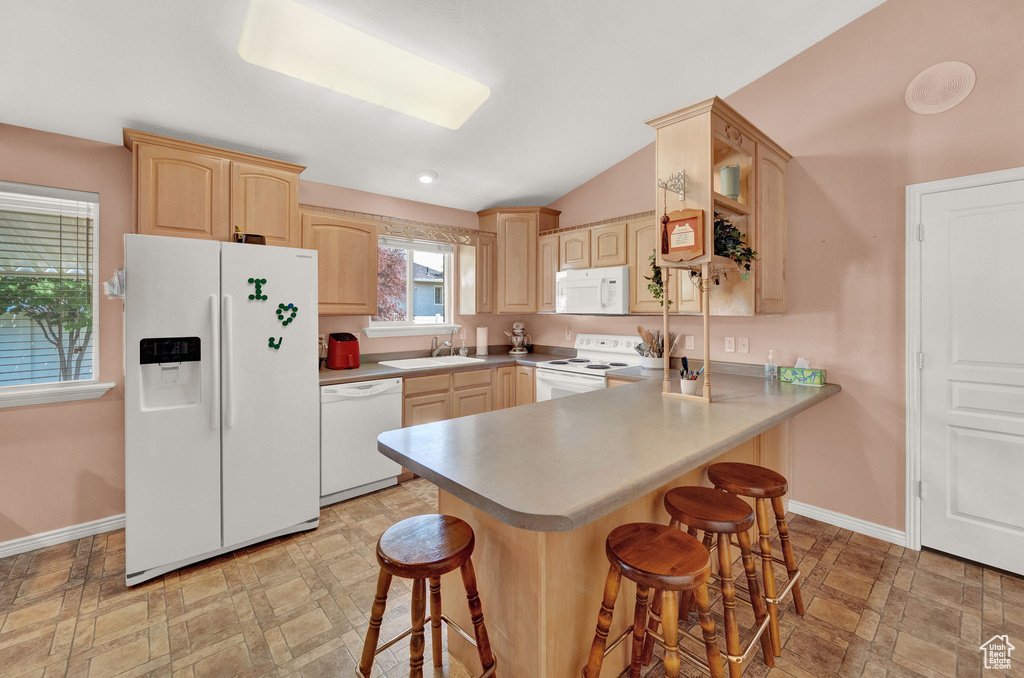 Kitchen featuring a breakfast bar area, sink, white appliances, and light brown cabinetry